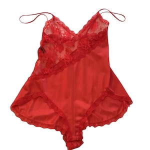 May include: A vibrant red bodysuit featuring a V-neckline with delicate floral lace detailing across the upper bodice. The garment includes thin spaghetti straps and a smooth satin-like fabric finish on the lower section, accented with matching lace trim along the leg openings.