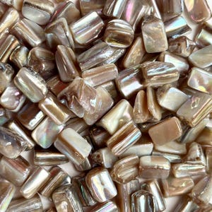 May include: A pile of iridescent rectangular beads in shades of brown, cream, and pearl. The beads have a glossy, polished appearance, reflecting light with a subtle rainbow sheen. These beads are suitable for jewelry making and crafting.