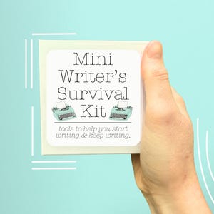 Könnte beinhalten: Eine cremefarbene Box mit der Aufschrift "Mini Writer's Survival Kit" wird vor einem hellblauen Hintergrund gehalten. Das Etikett zeigt eine Schreibmaschinen-Grafik und den Text "tools to help you start writing & keep writing."
