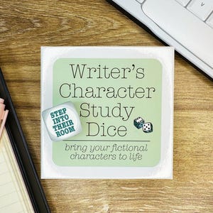 Könnte beinhalten: Eine quadratische weiße Karte mit einem hellgrünen Zentrum, das den schwarzen Text Writer's Character Study Dice, eine kleine Abbildung von zwei Würfeln und den Text bring your fictional characters to life enthält. Ein weißer Würfel mit dem Text STEP INTO THEIR ROOM liegt darauf.