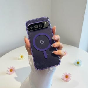 Può includere: Una custodia trasparente per telefono con un design glitterato viola e un anello magnetico viola con la lettera "G". La custodia è tenuta in mano, con una manica bianca visibile. Per Google Pixel 7.