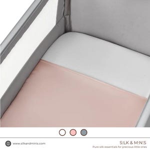 May include: A cot with a white fitted sheet and a blush pink silk blanket. The cot has a grey frame. The image also shows the website address silkandminis.com and the text "S:LK & M:N:S Pure silk essentials for precious little ones."