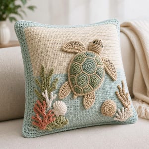 May include: A square crochet cushion featuring a sea turtle appliqué in shades of green and beige. The background is divided into beige and light blue sections, decorated with crocheted coral, seaweed, and seashell motifs in various colours.