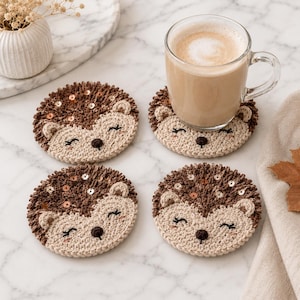 May include: Four round crochet coasters shaped like hedgehogs with dark brown textured backs featuring small copper sequins and light beige faces with embroidered closed eyes, small ears, and dark brown noses, one supporting a glass mug of coffee.