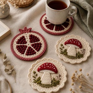 Könnte beinhalten: Gehäkelte Untersetzer in verschiedenen Designs. Ein Untersetzer hat die Form einer Granatapfelscheibe, andere zeigen rot-weiße Pilze mit grünen Blättern. Die Untersetzer sind aus cremefarbenem, rotem und grünem Garn gefertigt.
