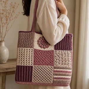 May include: A square crochet tote bag featuring a patchwork design of various textured squares in shades of cream, beige, mauve, and dark plum. The bag includes a central floral motif square and two long shoulder straps, all crafted from yarn.