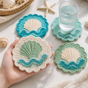 May include: Handmade crochet coasters in a seashell design. The coasters feature a scalloped edge and a seashell motif in shades of blue, green, and cream. One coaster holds a glass of water. The coasters are designed to protect surfaces from water rings.