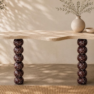 May include: A console table featuring a beige, organic-shaped travertine top supported by two vertical legs, each composed of five stacked, spherical dark brown marble spheres with white veining, creating a distinct contrast in colour and texture.