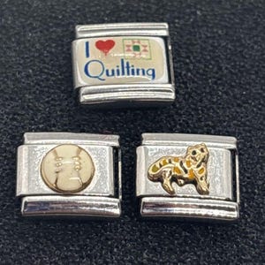 May include: Three silver charm bracelets with different designs. The first charm has a red heart with the words "I love quilting" on a white background. The second charm has a white baseball with black stitching. The third charm has a gold and yellow tiger design.