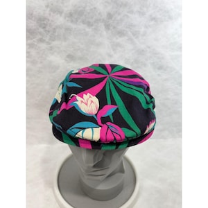 May include: A black newsboy cap with a vibrant floral pattern. The design features pink, green, and purple stylized flowers and leaves. The cap is displayed on a gray mannequin head.