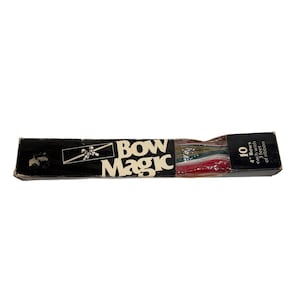 May include: A rectangular black box labeled Bow Magic containing 10 bows, each with 3 feet of ribbon. The packaging features white text and a graphic of a gift box with a bow. The contents include multi-colored ribbons visible through a clear window.