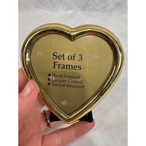 Può includere: Un set di cornici per foto a forma di cuore, color oro. La cornice ha una finitura lucida ed è laccata. Il testo sulla cornice recita "Set of 3 Frames". La cornice è resistente all'ossidazione.