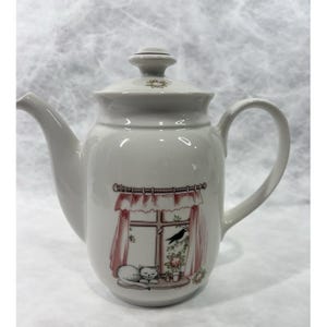 May include: White ceramic teapot with a lid and curved handle. The teapot features a decorative illustration of a window with a cat, a bird, and floral accents. The spout is curved, and the lid has a small floral design.