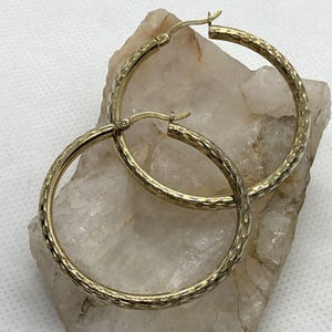 May include: A pair of gold hoop earrings with a textured finish. The earrings are large and circular.