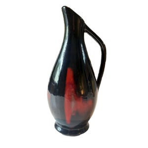 May include: A tall, black ceramic pitcher with a curved handle and a flared spout. The pitcher features a glossy finish with vertical red streaks. The base is a darker shade of black. This decorative pitcher is suitable for serving beverages.