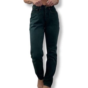 May include: Dark green denim jeans with a high waist and a classic five-pocket design. The jeans have a button and zipper closure and a straight leg fit. The fabric appears to be a medium weight denim.
