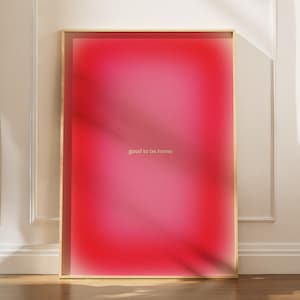Könnte beinhalten: Ein gerahmter Kunstdruck mit einem Farbverlauf aus Rosa- und Rottönen. Der Text "good to be home" ist hell zentriert. Der Rahmen ist goldfarben, und das Kunstwerk lehnt an einer weißen Wand mit Leisten.