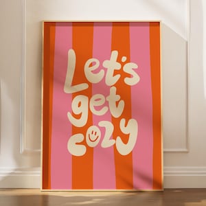 Könnte beinhalten: Ein gerahmter Kunstdruck mit einem vertikal gestreiften Hintergrund in Orange und Rosa. Die Worte "Let's get cozy" sind in einer verspielten, cremefarbenen Schrift geschrieben, mit einem Smiley anstelle des "o" in "cozy".
