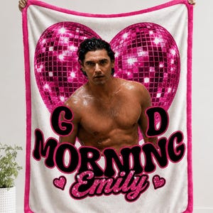May include: A white fleece blanket with a bright pink border featuring a large heart-shaped pink disco ball graphic behind a shirtless man. The text reads GOOD MORNING in bold black letters and Emily in pink glitter script with two small pink hearts.