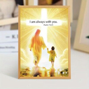 May include: Framed art print featuring a religious scene with a figure in a yellow robe holding the hand of a child. The background is a bright, golden light with the text "I am always with you." and "Psalm 73:23". The frame is made of light-colored wood.