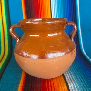 May include: A white ceramic mug with a black handle and the text "But First, Coffee" in a black, bold font. The mug is on a white surface.