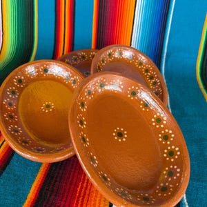 May include: A set of three oval-shaped terracotta bowls with a smooth, glazed finish. Each bowl features a warm brown base color and is decorated with a repeating pattern of small white dots and green centers along the inner rim and center.