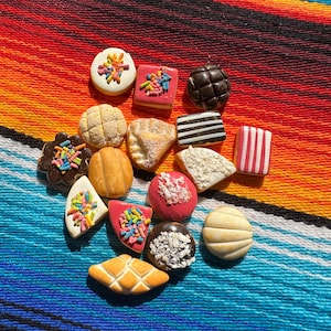 May include: A collection of colorful, miniature baked goods and candies, including cookies, pastries, and chocolates, arranged on a vibrant, striped textile. The treats feature various shapes, colors, and decorative toppings.