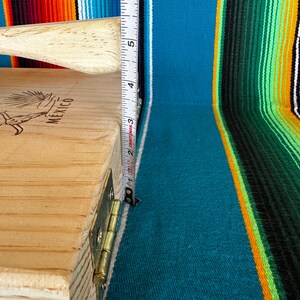 Puede incluir: Prensa para tortillas de madera clara con mango. La prensa mide aproximadamente 13 cm de alto. La palabra "MEXICO" es visible en el lateral. El fondo es un textil a rayas colorido.