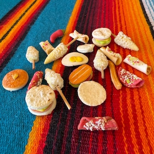 May include: A collection of miniature food items including small sandwiches, corn on the cob on sticks, tacos, and various round pastries. The items feature textures and colors representing bread, meat, vegetables, and toppings in a variety of shapes.