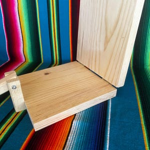Puede incluir: Una prensa de tortillas de madera clara, con una base rectangular y una tapa con bisagras. La prensa est&aacute; hecha de madera sin terminar y est&aacute; dise&ntilde;ada para hacer tortillas. El fondo es un textil a rayas de colores.