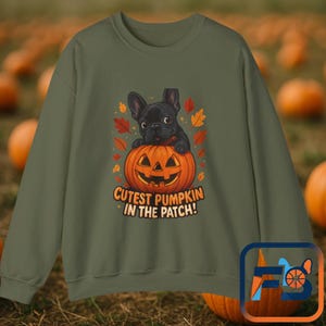 May include: Khaki green sweatshirt with a graphic of a black French bulldog puppy on an orange carved pumpkin. The pumpkin has a smiling face and is surrounded by autumn leaves. Text reads "Cutest Pumpkin in the Patch!"