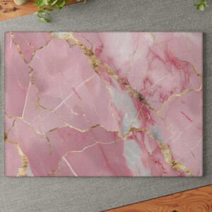 Op de afbeelding: Een rechthoekige roze marmeren snijplank met gouden adering. De plank heeft een gepolijst oppervlak en een natuurlijk steenpatroon. De roze kleur wordt geaccentueerd door witte en gouden strepen, wat een luxe uitstraling creëert. Ideaal voor de keuken.