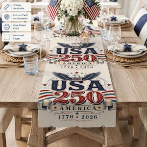 Puede incluir: Camino de mesa color crema con diseño patriótico. Presenta el texto "USA 250 AMERICA 1776-2026" con un emblema de águila y detalles en rojo, blanco y azul. El camino de mesa está sobre una mesa de madera.