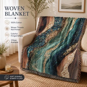 May include: A woven blanket featuring an abstract agate-inspired pattern in shades of teal, deep blue, brown, and gold. The blanket has fringed edges and is made of 100% cotton. Text on the image includes WOVEN BLANKET, 100% Cotton, Woven Threads Not Printed, Colorful Fringed Edges, 3 Sizes Available, and SOFT, DURABLE & MADE TO LAST.