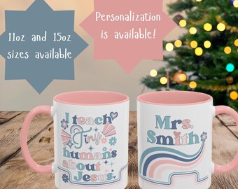 May include: Two white ceramic mugs with pink handles and interiors. One mug reads "I teach tiny humans about Jesus" in a retro font. The other mug says "Mrs. Smith" with a retro design. The mugs are available in 11oz and 15oz sizes.