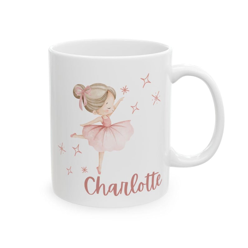May include: White ceramic mug featuring a watercolor illustration of a ballerina in a pink tutu and the name "Charlotte" in a matching script. The design includes stars and sparkles, creating a whimsical aesthetic.