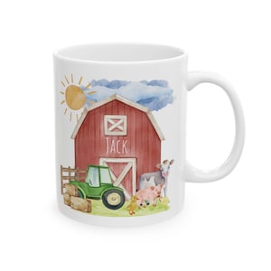 May include: White ceramic mug featuring a watercolor illustration of a red barn, green tractor, and farm animals. The name "JACK" is printed on the barn. A yellow sun and blue clouds complete the farm scene.