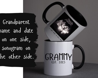 May include: Two white ceramic mugs with black handles and rims. One mug displays the word "GRAMMY" and "EST. 2025". The other mug has a sonogram image and the text "I CAN'T WAIT TO MEET YOU". The image suggests a pregnancy announcement.