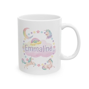 May include: White ceramic mug featuring a whimsical design with unicorns, a rainbow, and stars. The name "Emmaline" is displayed in a pink cloud. The mug has a curved handle.
