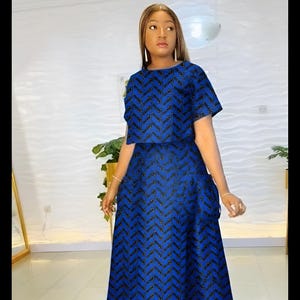 May include: A two-piece blue outfit with a chevron pattern. The top is a short-sleeved crop top, and the skirt is a floor-length skirt with a small train. The outfit is decorated with black accents.