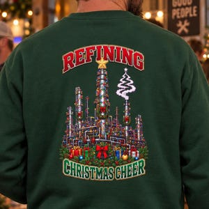May include: A dark green crewneck sweatshirt featuring a back graphic of an industrial oil refinery decorated with Christmas lights, wreaths, and presents. The text REFINING is arched above, and CHRISTMAS CHEER is printed below the refinery illustration.