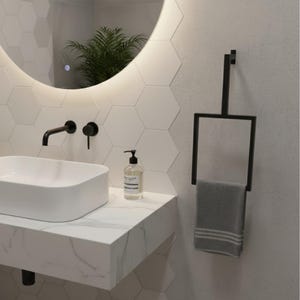 May include: A modern bathroom scene featuring a white rectangular sink, black faucet, and a black towel rack with a gray towel. The wall is decorated with white hexagonal tiles and a round mirror with a soft glow.