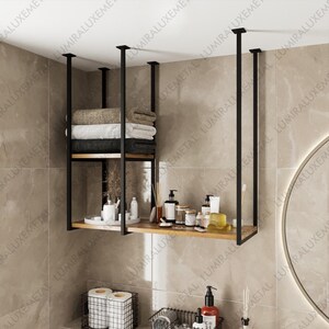 May include: A black metal and wood floating shelf unit suspended from the ceiling. The shelves hold folded towels, toiletries, and decorative items. The unit is in a bathroom setting.