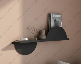 May include: A modern black wall shelf with a semi-circular design. The shelf holds a book with the word "WELCOME" on the cover, a small vase, and decorative items. The shelf is mounted on a peach-colored wall.