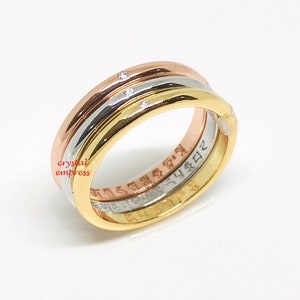Può includere: Un anello a tre bande con finitura oro rosa, oro bianco e oro giallo. L'anello ha un piccolo diamante incastonato in ogni banda. L'anello è inciso con le parole "crystal empress" all'interno.
