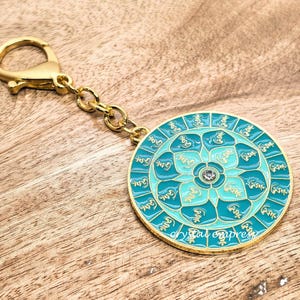 May include: A gold-colored keychain with a round, teal and gold pendant. The pendant features a floral design with a central jewel and the text "crystal empress". The keychain has a lobster clasp and chain.