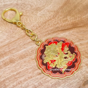 May include: Gold keyring with a red and gold circular charm featuring a detailed design of a dragon with the text "crystalexpress".