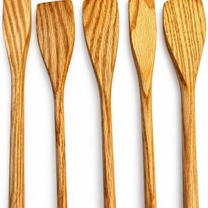 May include: A set of five wooden kitchen spatulas arranged vertically. Each utensil features a long, slender handle and a flat, wide head with a distinct light brown wood grain pattern visible throughout the surface of the natural material.