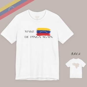 May include: White t-shirt with the text "MAKE DE PINGA AGAIN" and a colorful design resembling the Venezuelan flag. The back of the shirt shows a silhouette of Venezuela. The shirt has short sleeves and a crew neck.
