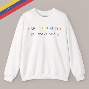 May include: White crew neck sweatshirt with the text "MAKE VENEZUELA DE PINGA AGAIN" in colorful letters. The Venezuelan flag is in the upper left corner. The sweatshirt has long sleeves and a relaxed fit.